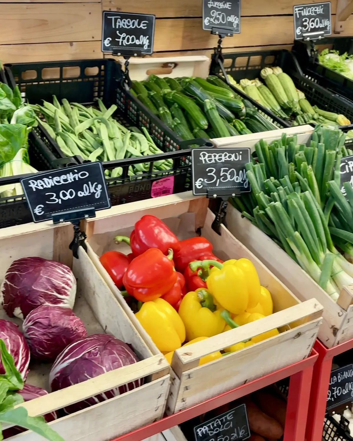 Cassette di legno con radicchio, peperoni rossi e gialli, fagiolini, zucchine e cipollotti nel punto vendita di un'azienda agricola, con i prezzi scritti a gesso